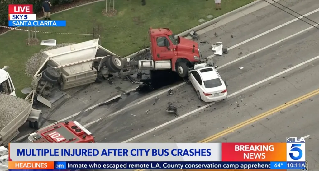 Overhead view of a bus crash involving a red semi-truck, a white car, and an overturned trailer, with debris scattered on the road.
