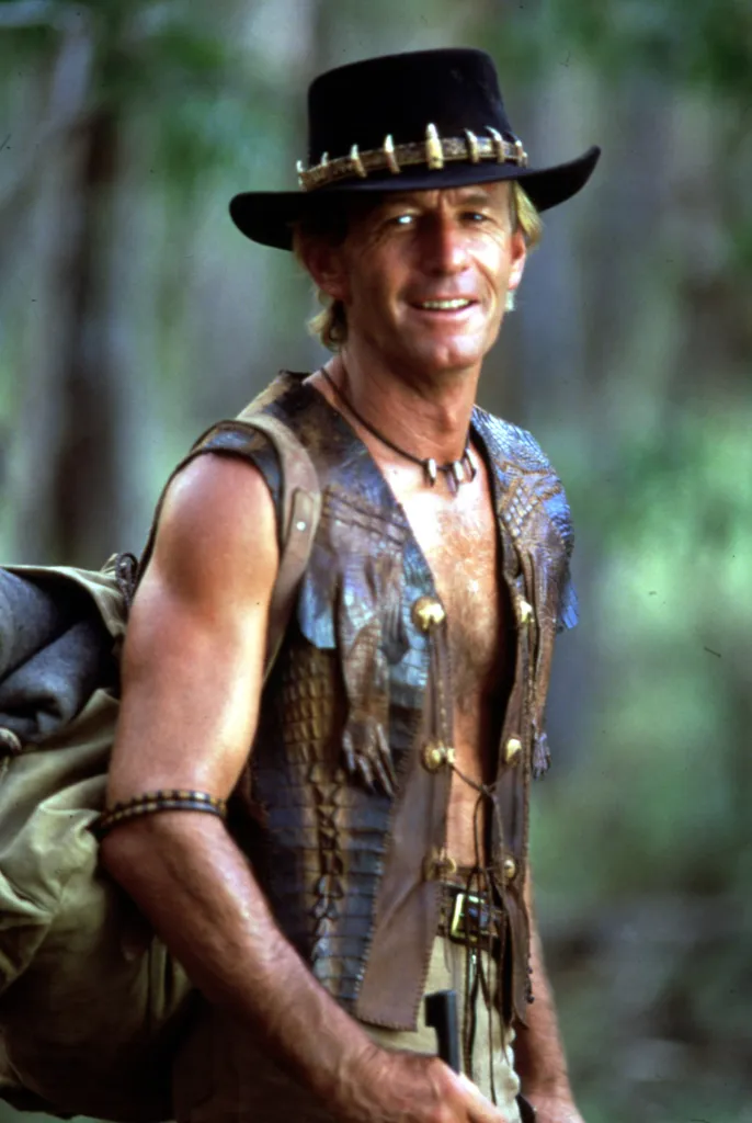 Paul Hogan as Crocodile Dundee, wearing a crocodile-tooth hat and vest, and carrying a rucksack.