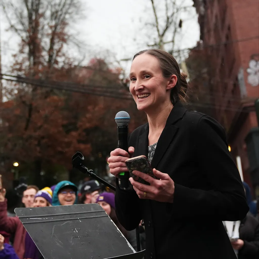 Seattle Mayor-elect Katie Wilson smiles while speaking into a microphone at a Starbucks strike.