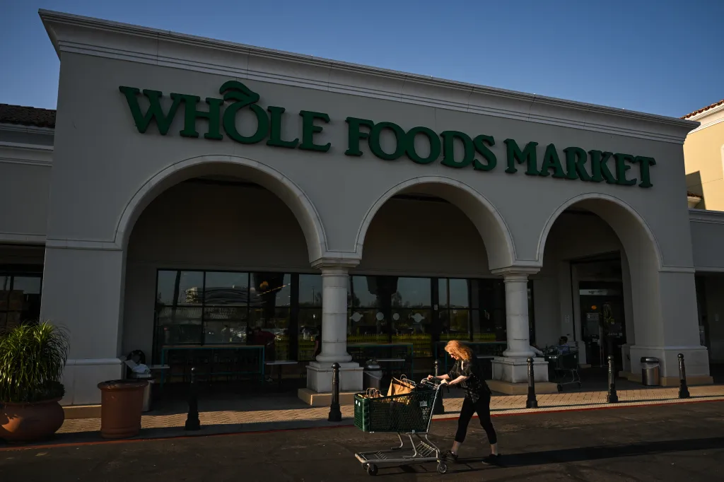 A customer pushing a shopping cart filled with bags outside a Whole Foods Market.