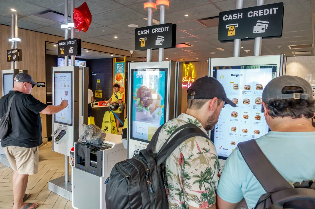 Customers ordering from touchscreen kiosks inside a McDonald's.