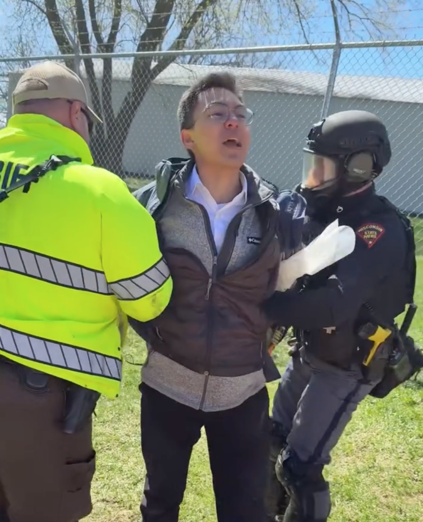 Dean Guzman Wyrzykowski being arrested by two law enforcement officers.