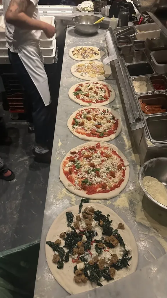 Pizzas being prepared at Del Popolo, with toppings like sausage, kale, and cheese.