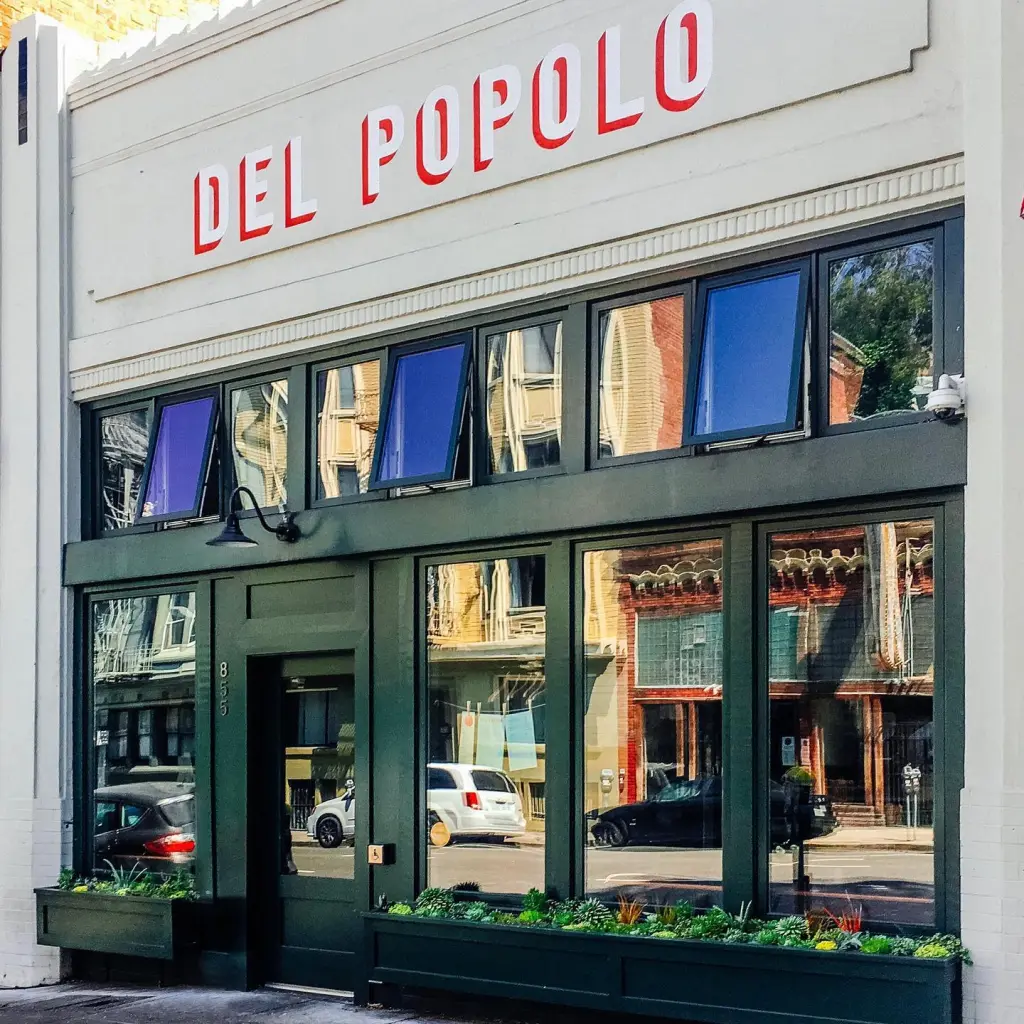Exterior of Del Popolo pizzeria with its name in red letters above dark green windows and door.