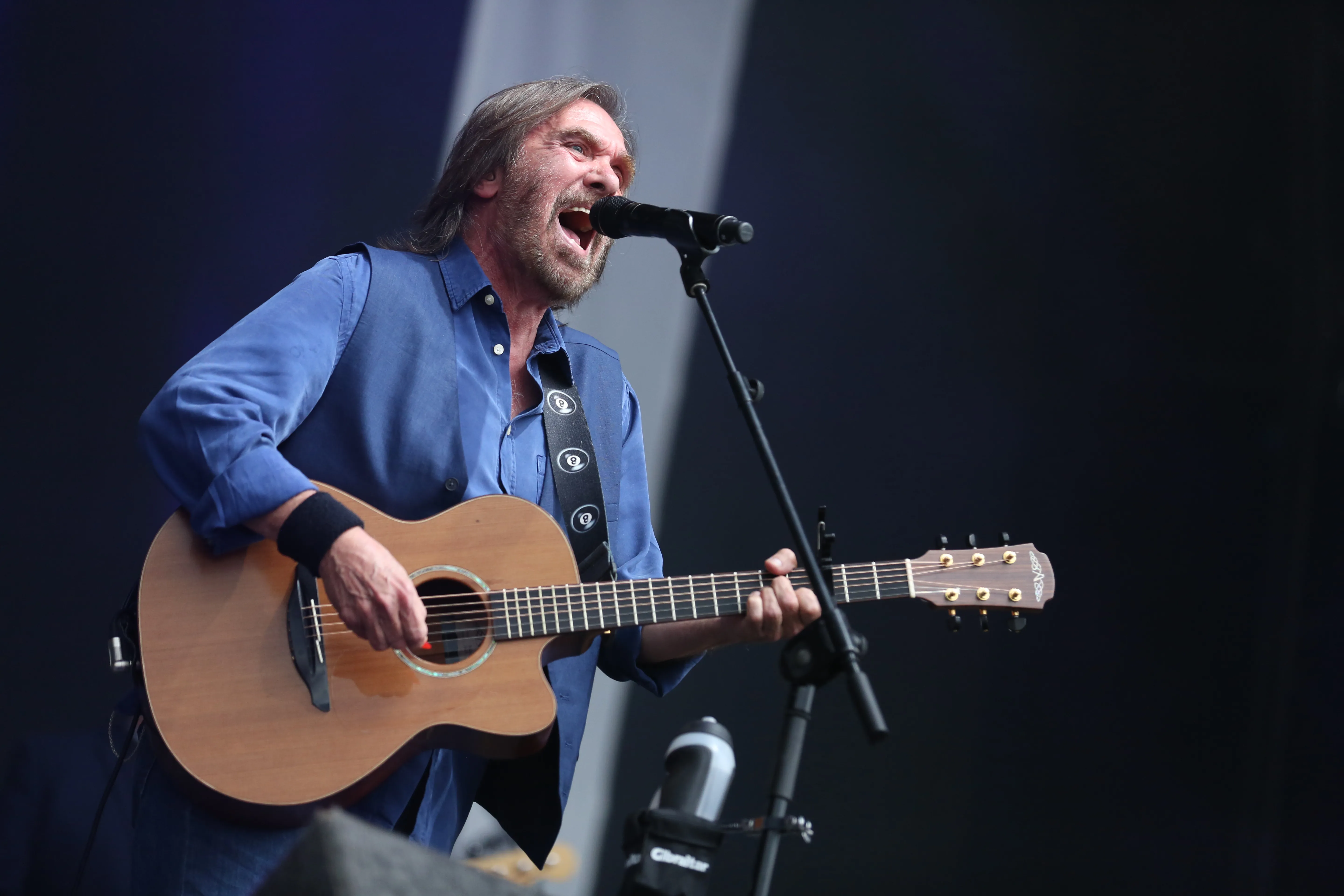 Dennis Locorriere of Dr. Hook singing into a microphone while playing an acoustic guitar.
