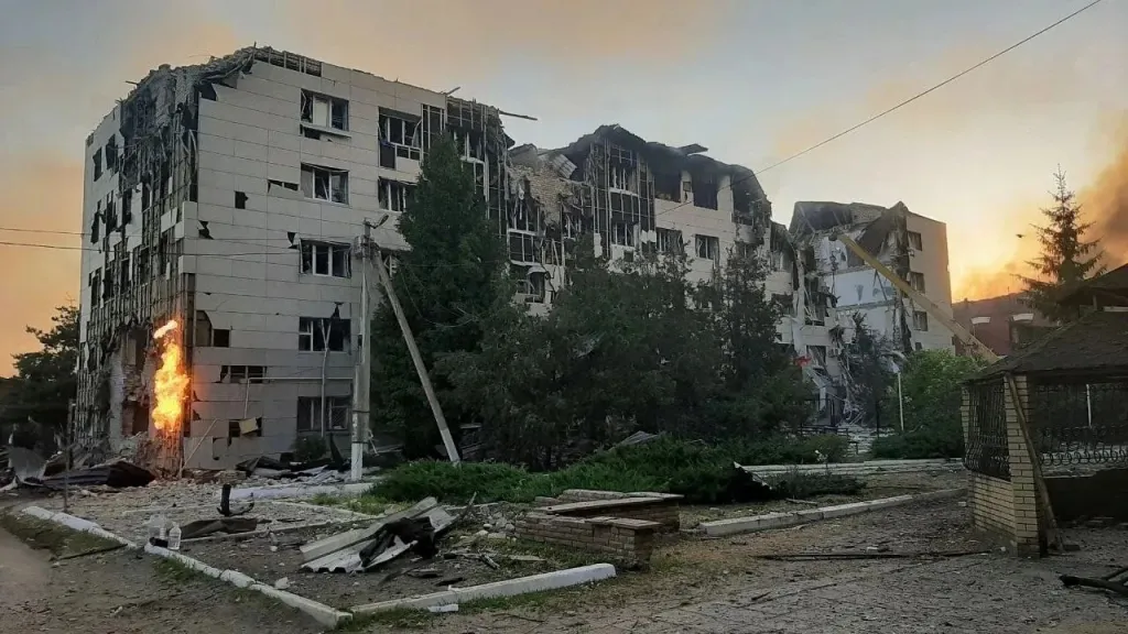 The aftermath of a drone attack on a Luhansk dormitory, showing a heavily damaged building with visible flames and smoke.