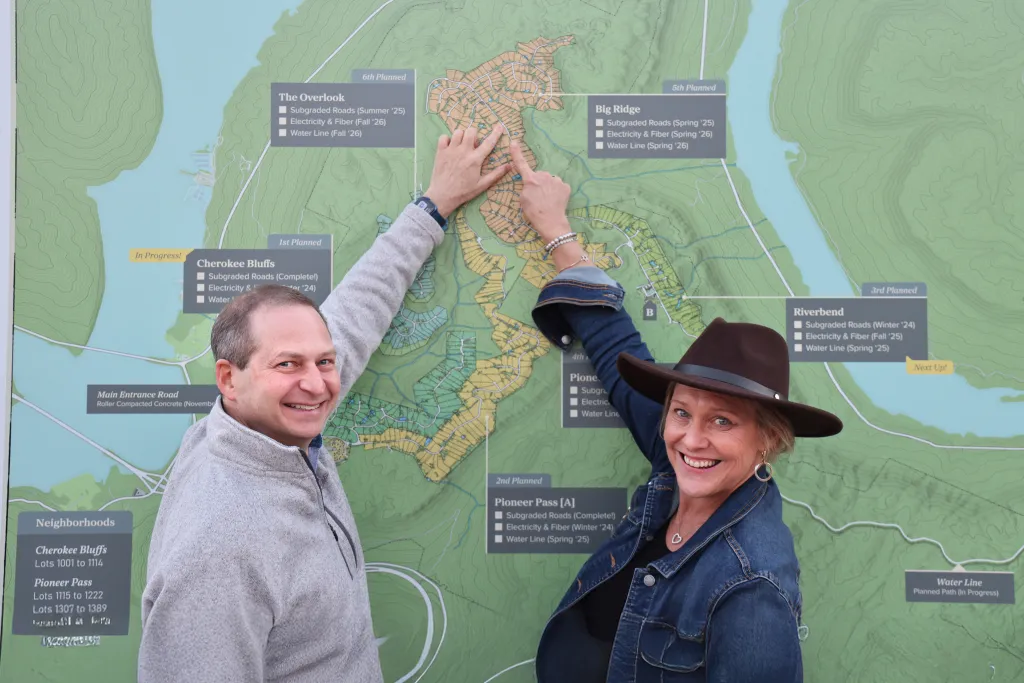 Two people smile at the camera while pointing at a development map with areas labeled 