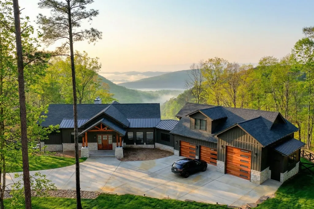 A modern house with a paved driveway and black car, nestled in green mountains with mist in the valley.