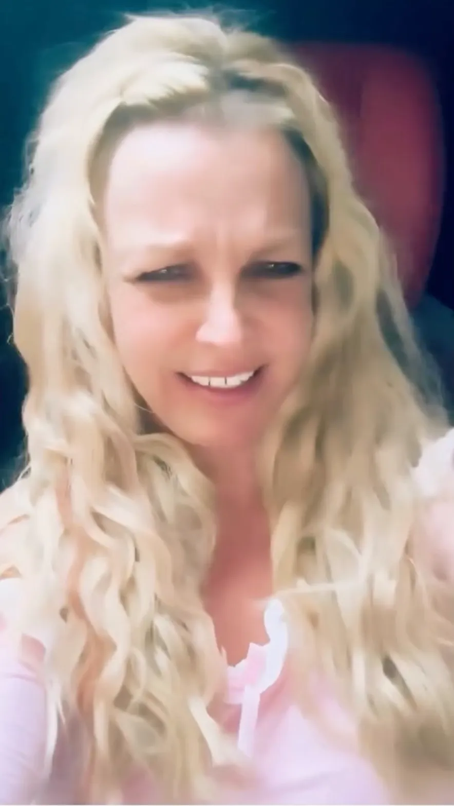 Britney Spears with a confused expression, long wavy blonde hair, and wearing a pink top.
