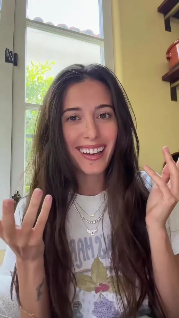 Lexi Manzo smiling at the camera, wearing a necklace with the word