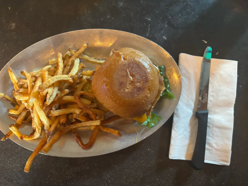 An overhead shot of a burger and fries on an oval metal plate, with a serrated knife on a white paper napkin beside it.