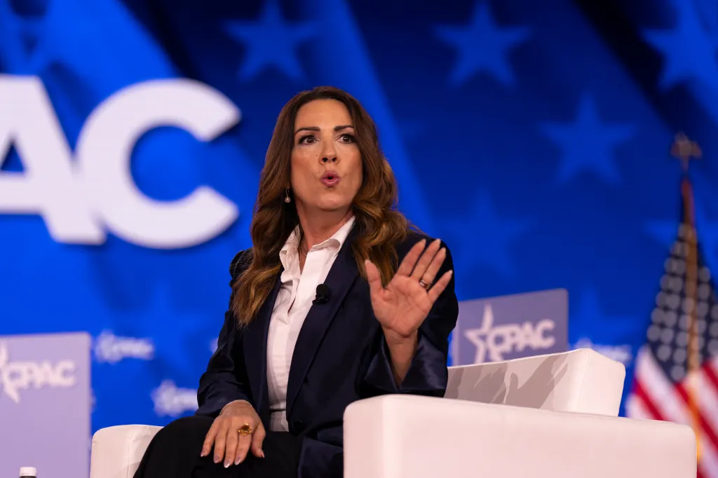 Sara Carter speaking at CPAC in Dallas, with a large CPAC logo behind her.