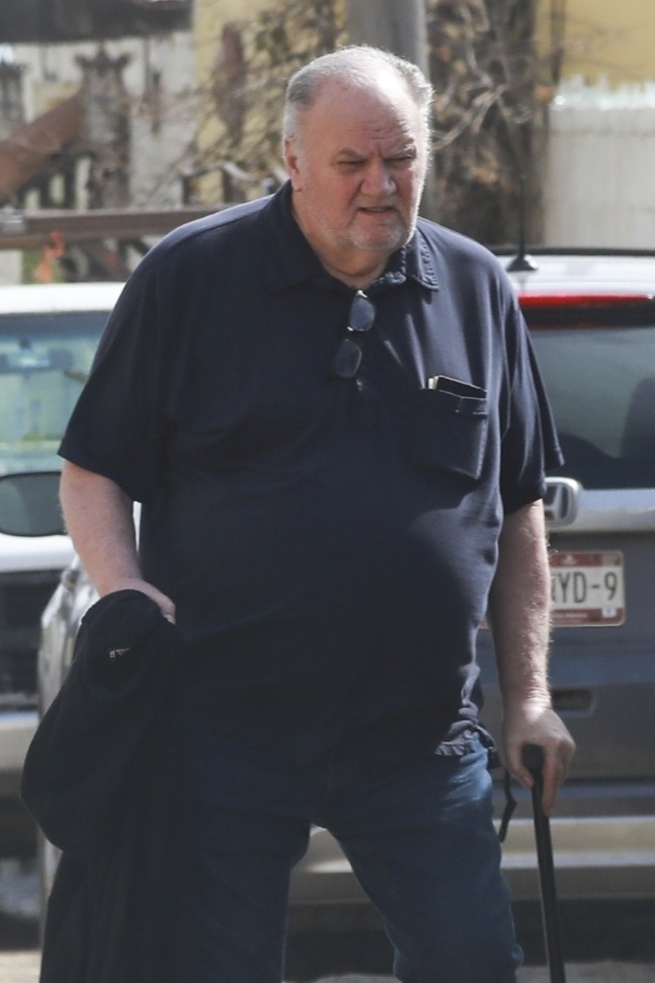 Thomas Markle walking out of his Rosarito residence, holding a cane and wearing a dark blue polo shirt.