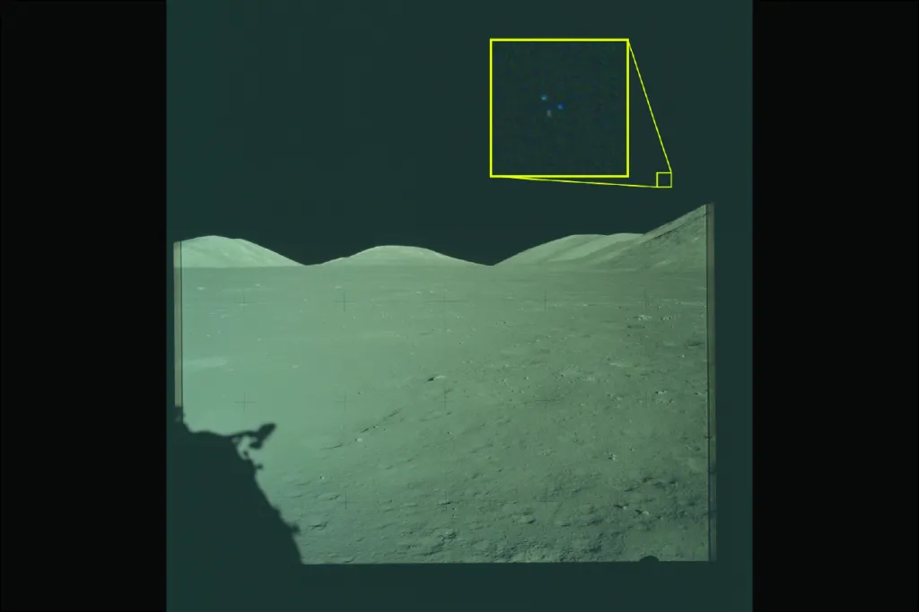 A wide-angle photo of a lunar landscape with small hills in the background under a dark sky, and a zoomed-in inset in the upper right showing a blurry cluster of blue, white, and red dots.