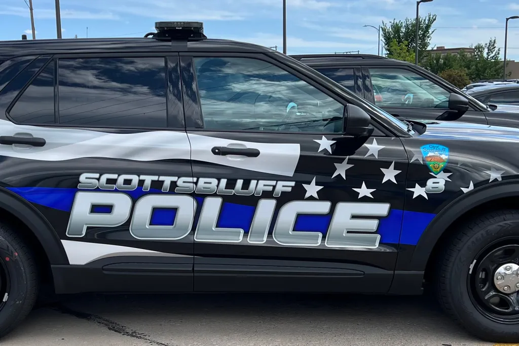 Black Scottsbluff Police vehicle with blue and white stripes, stars, and the city logo.