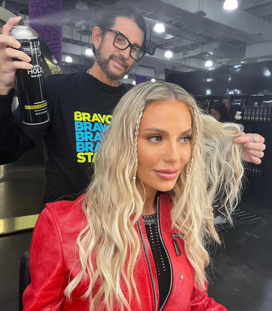 Dorit Kemsley getting her hair styled by a man holding hairspray.