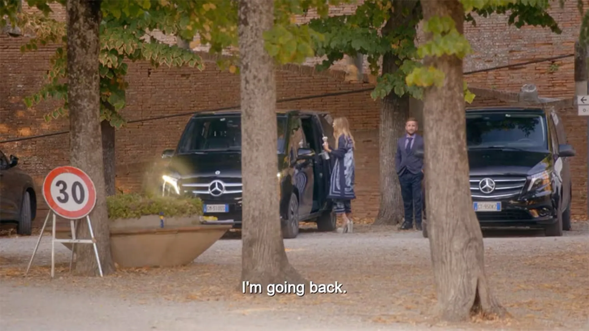 Dorit Kemsley gets out of a black Mercedes van in Italy as a man in a suit stands by a second black Mercedes van.