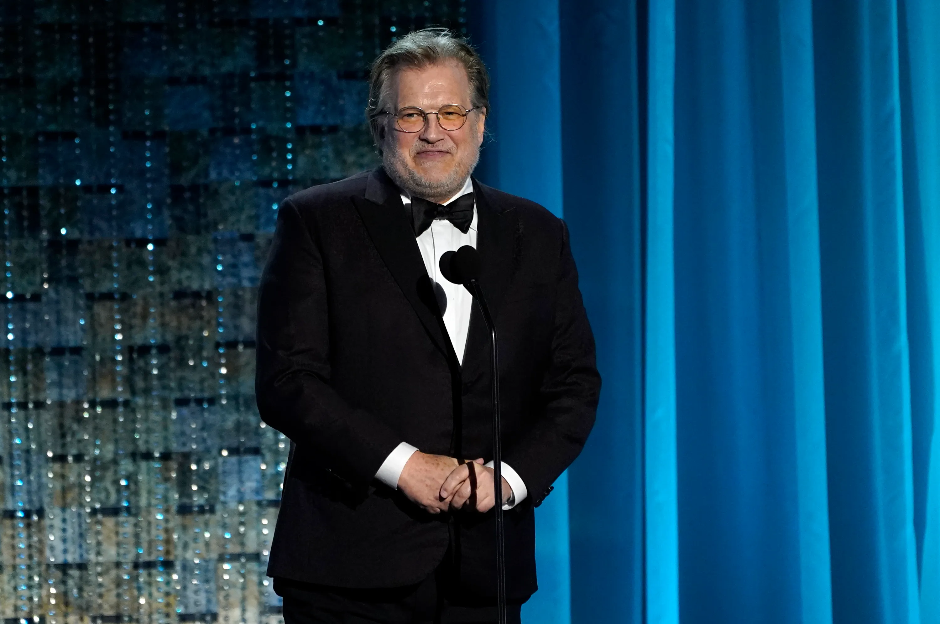 Drew Carey speaking at a podium.