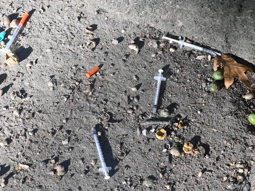 Four discarded syringes lie on the ground among small debris.
