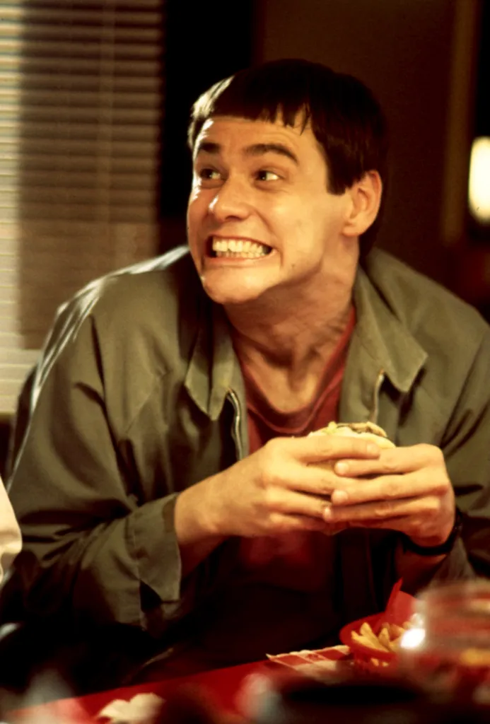 Jim Carrey as Lloyd Christmas making a face while holding a hamburger in 