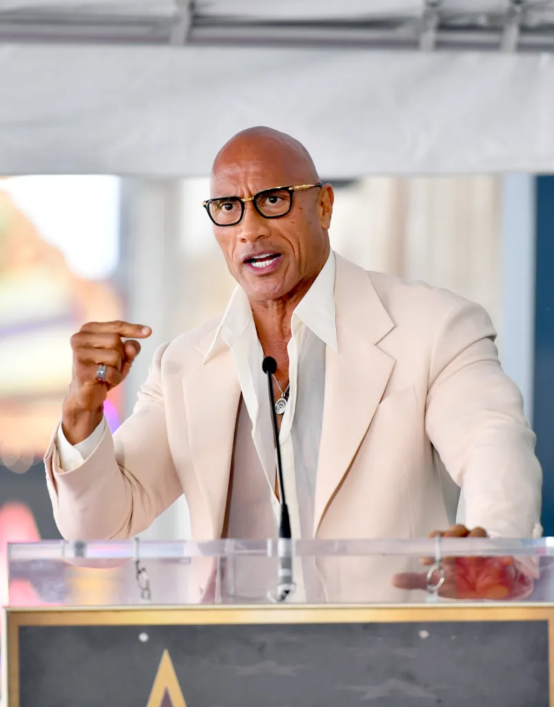 Dwayne Johnson speaking at a podium with a microphone.