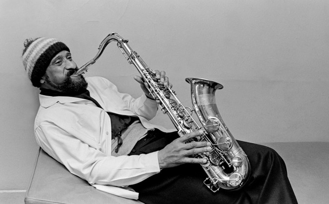 Sonny Rollins wearing a wool beanie, playing the sax on a sofa