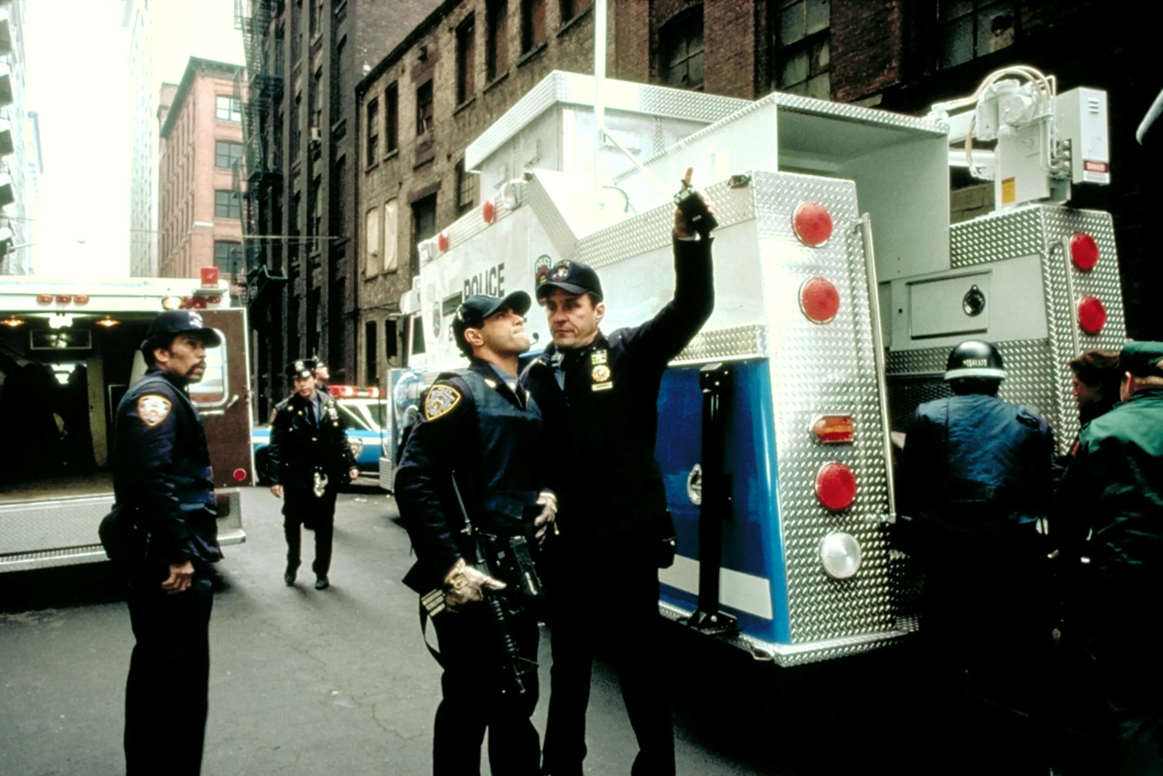 Beau Starr and Eddie Velez looking up while standing near a police truck in a scene from 