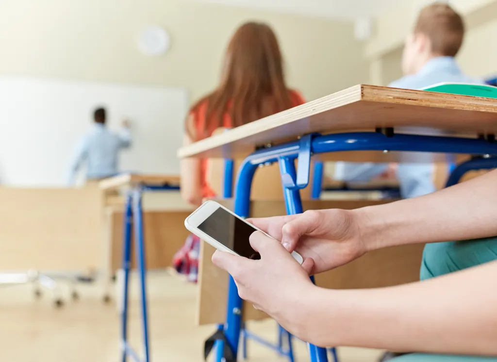 Student texting on a smartphone under a desk during a lesson.