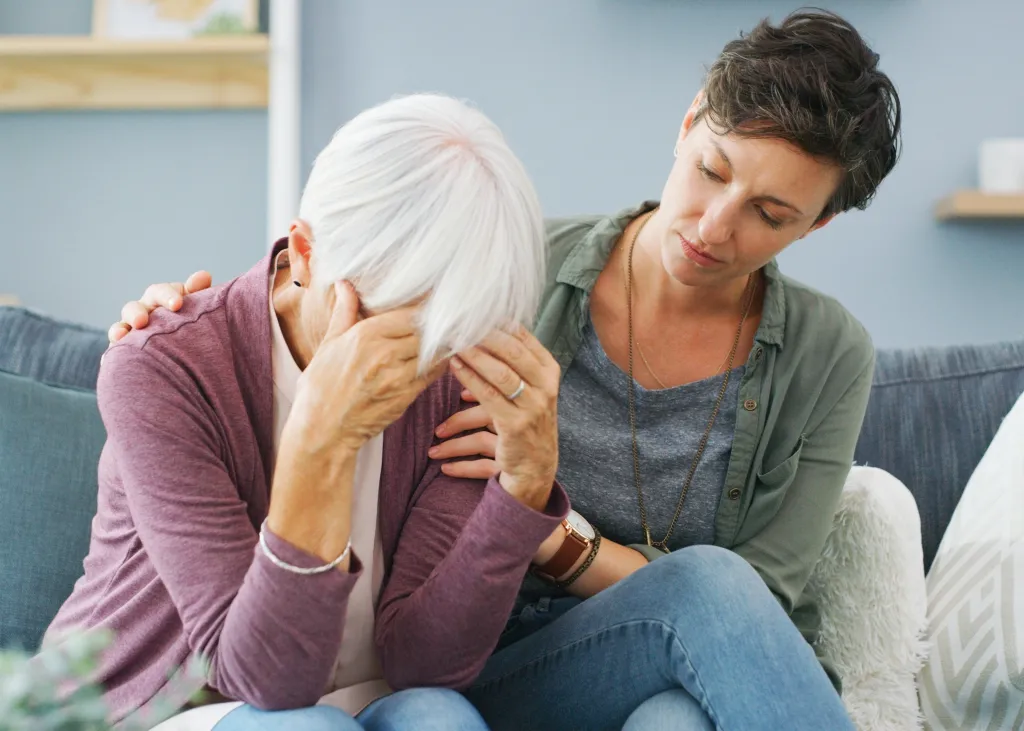 A younger woman comforting an older woman who is distressed, sitting together on a sofa.