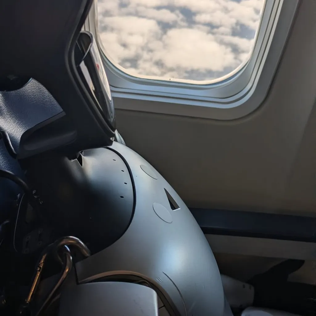 A robot looking out of an airplane window at the clouds.