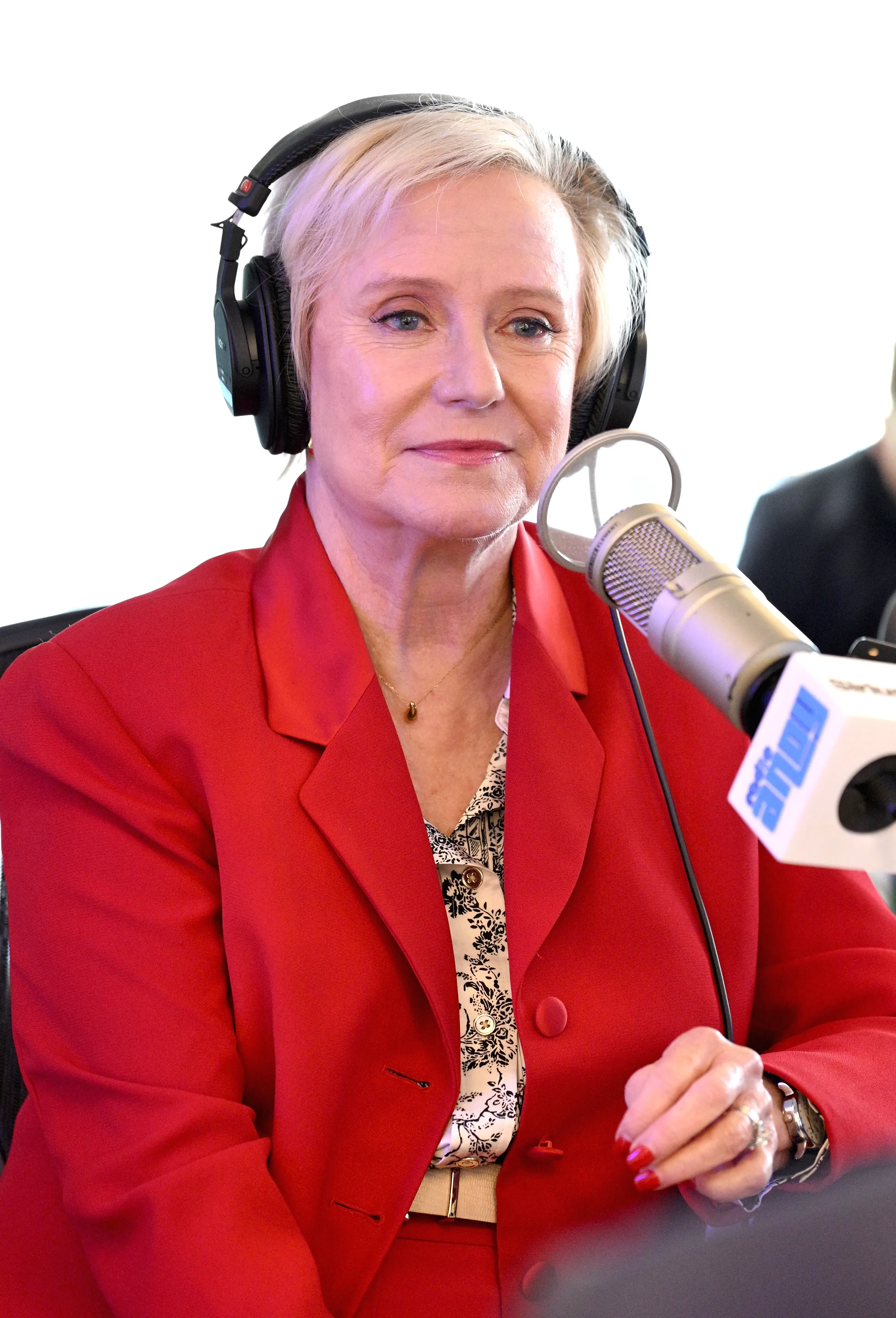 Eve Plumb in a red suit wearing headphones and speaking into a microphone.
