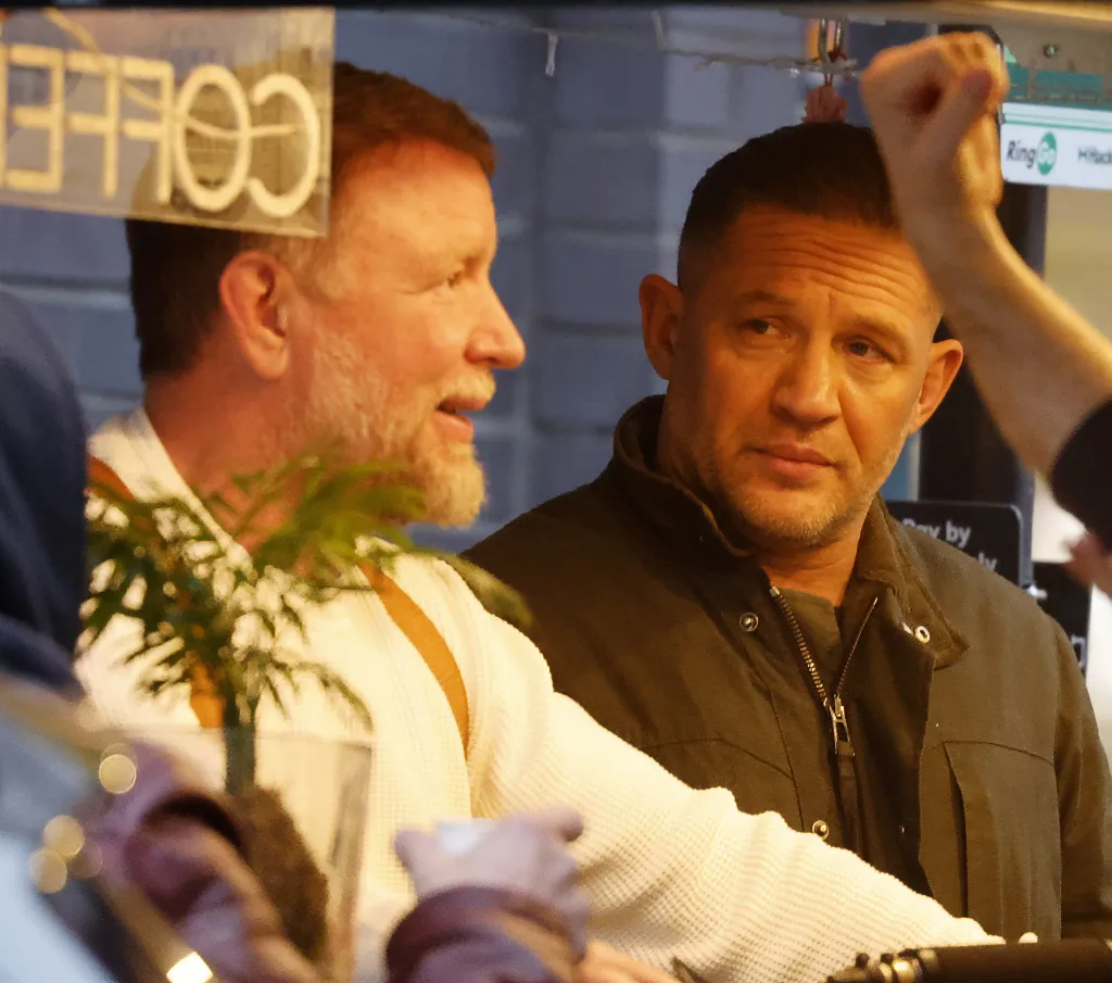 Tom Hardy filming a scene for MobLand Season 2, looking over his shoulder at another man.