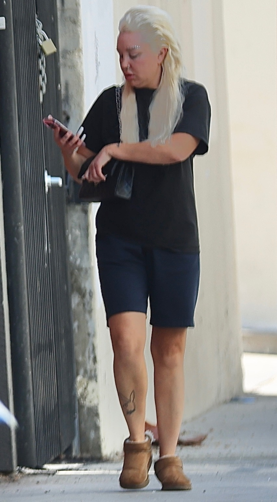 Amanda Bynes with platinum-blonde hair and jeweled eyebrows, wearing a black t-shirt, dark shorts, and Ugg boots, holding a pack of Marlboro cigarettes and a phone.
