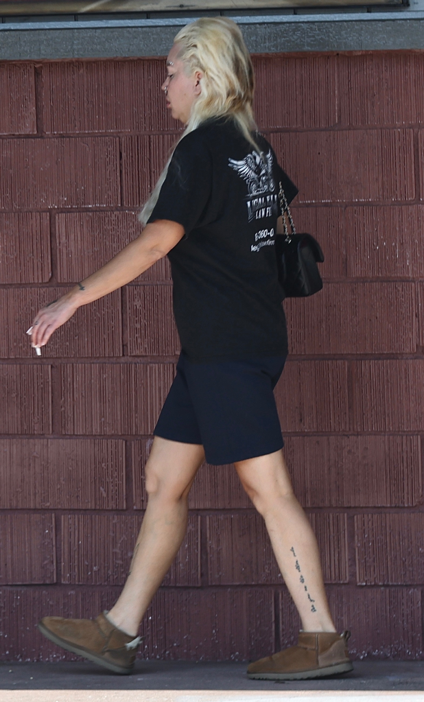 Amanda Bynes walking in a black t-shirt and shorts, with platinum blonde hair, jeweled eyebrows, and a pack of Marlboro cigarettes in her hand.