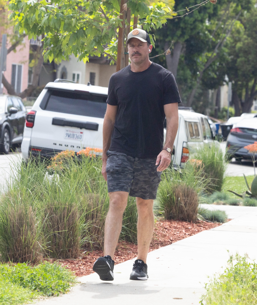 Armie Hammer in a black tee, camo shorts, and a baseball cap, walking down a street in West Hollywood.