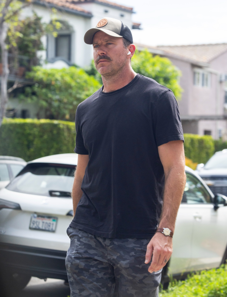 Armie Hammer wearing a baseball cap, black tee, and camo shorts while walking in West Hollywood.