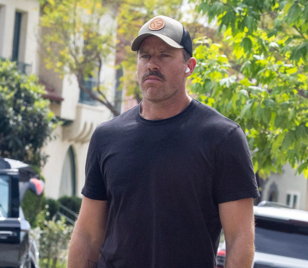 Armie Hammer wearing a baseball cap, black t-shirt, and mustache.