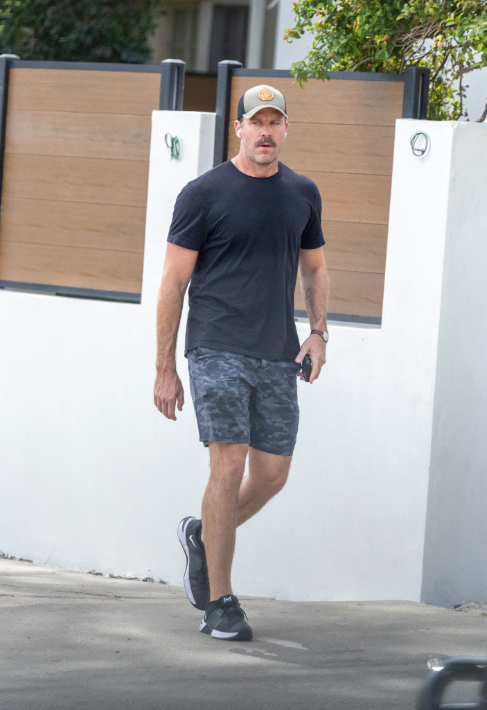 Armie Hammer in a black tee, camo shorts, and a baseball cap walking in West Hollywood.