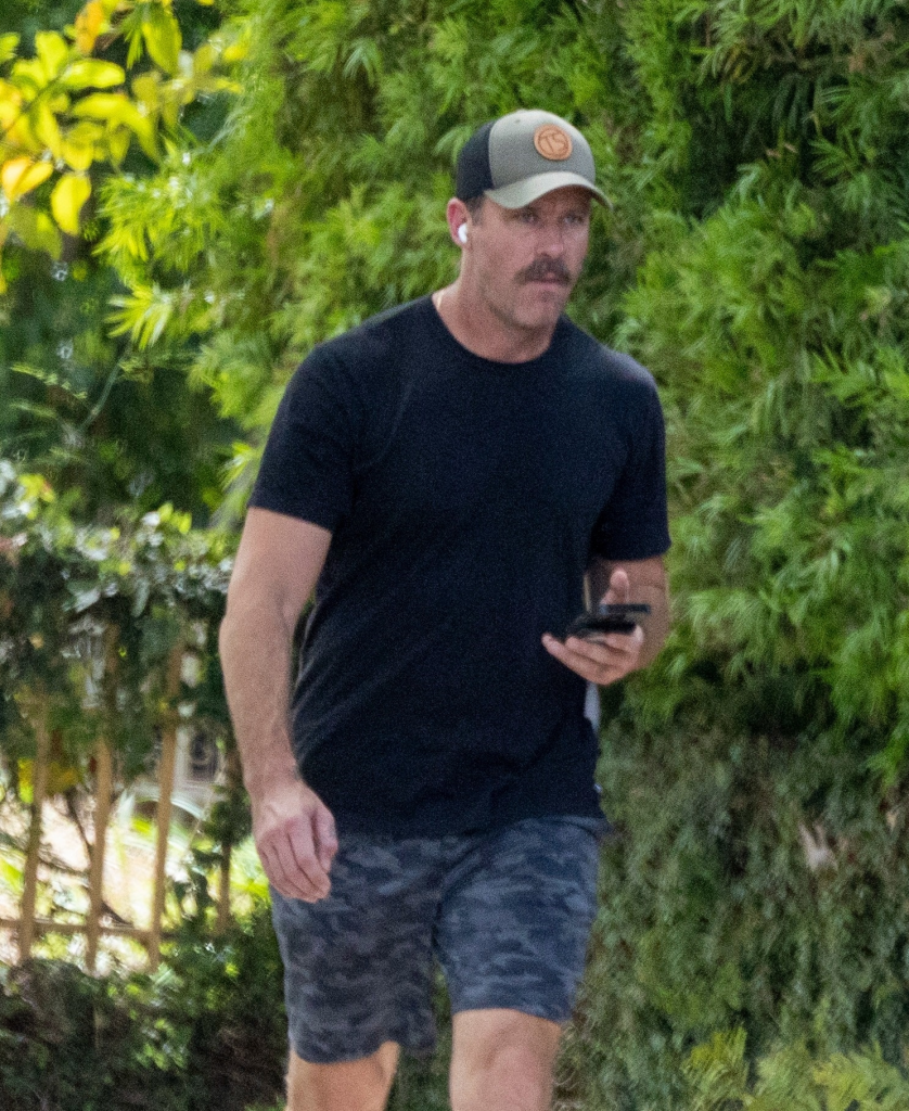 Armie Hammer wearing a baseball cap, black t-shirt, and camo shorts while walking.