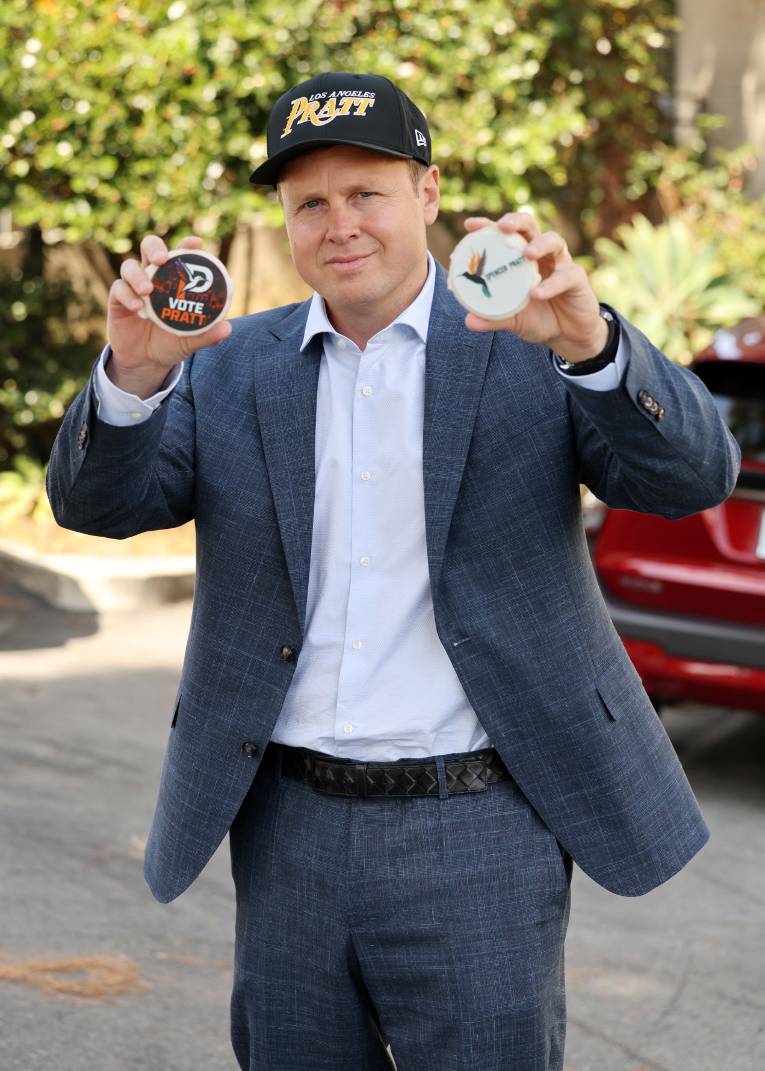 Spencer Pratt in a blue suit and black baseball cap, holding two 