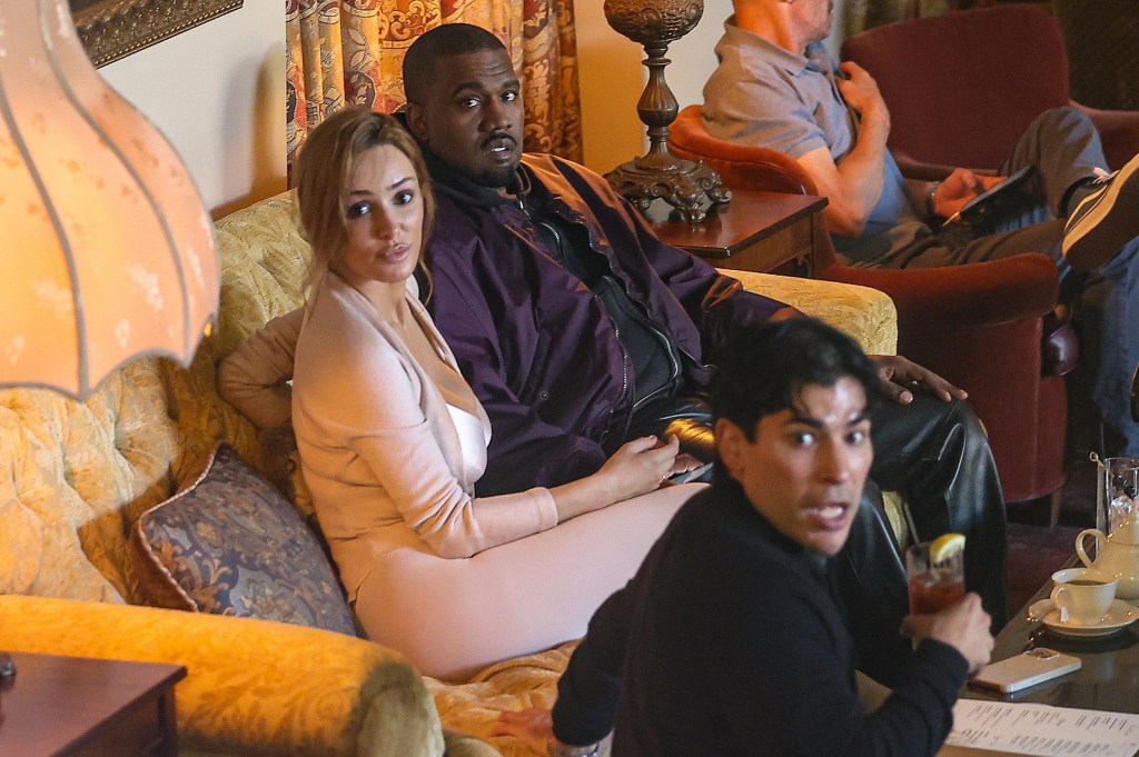 Kanye West and Bianca Censori sit on a sofa at Chateau Marmont with another person, with Censori wearing a light pink outfit and West in a purple jacket.