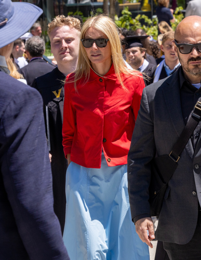 Gwyneth Paltrow in a red shirt and light blue skirt, walking with a group of people.