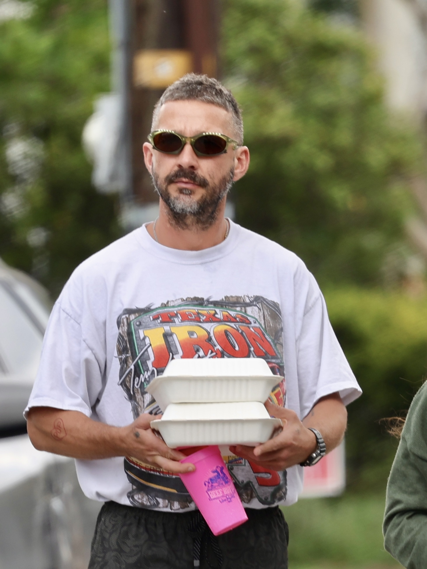 Shia LaBeouf carrying takeout containers and a pink cup.