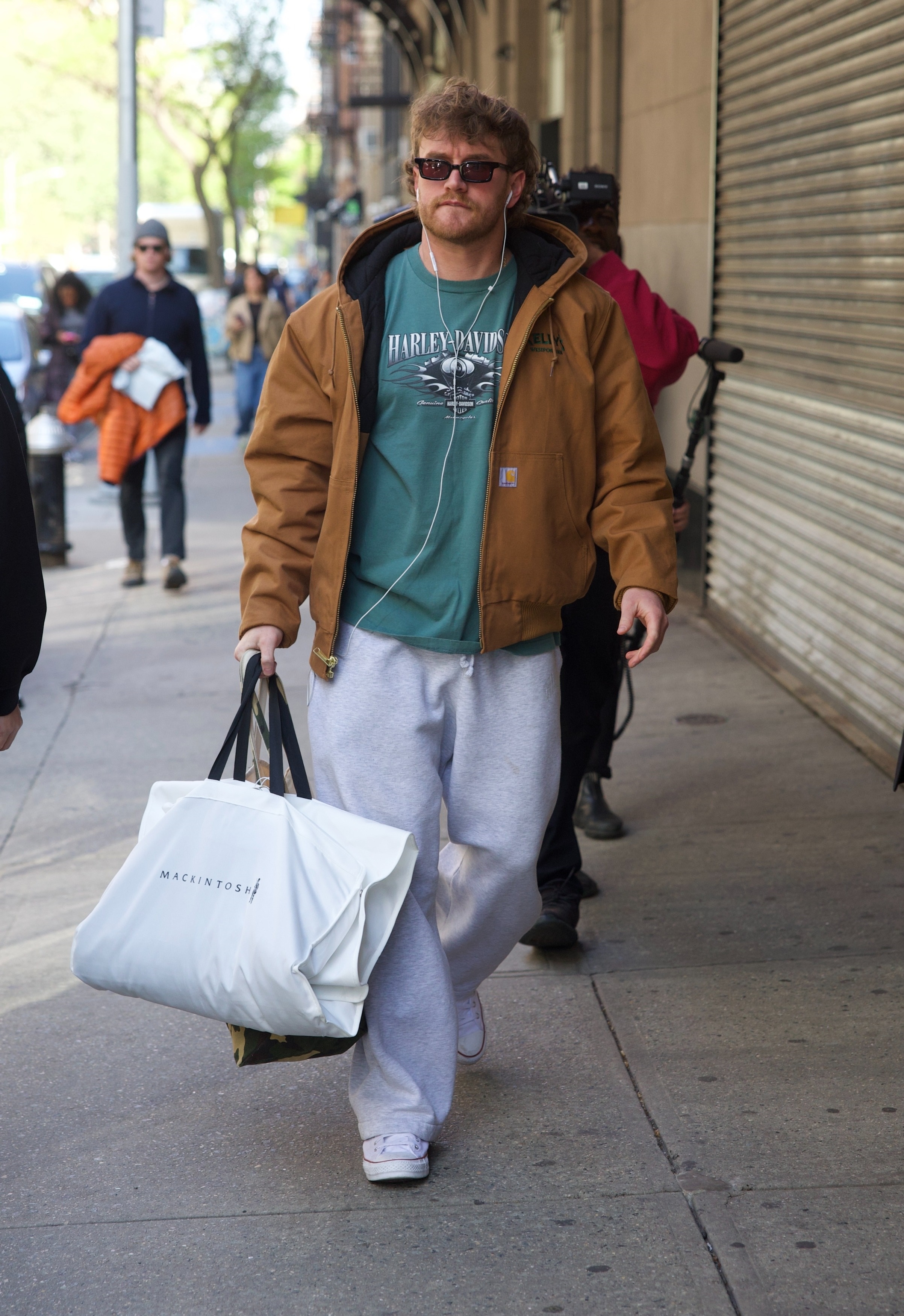 West Wilson walking on a city sidewalk carrying a white Mackintosh bag.