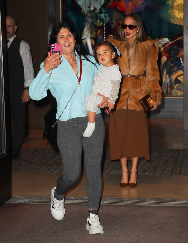 Jennifer Lopez appearing amused as a woman holding a child walks in front of cameras, blocking the view.
