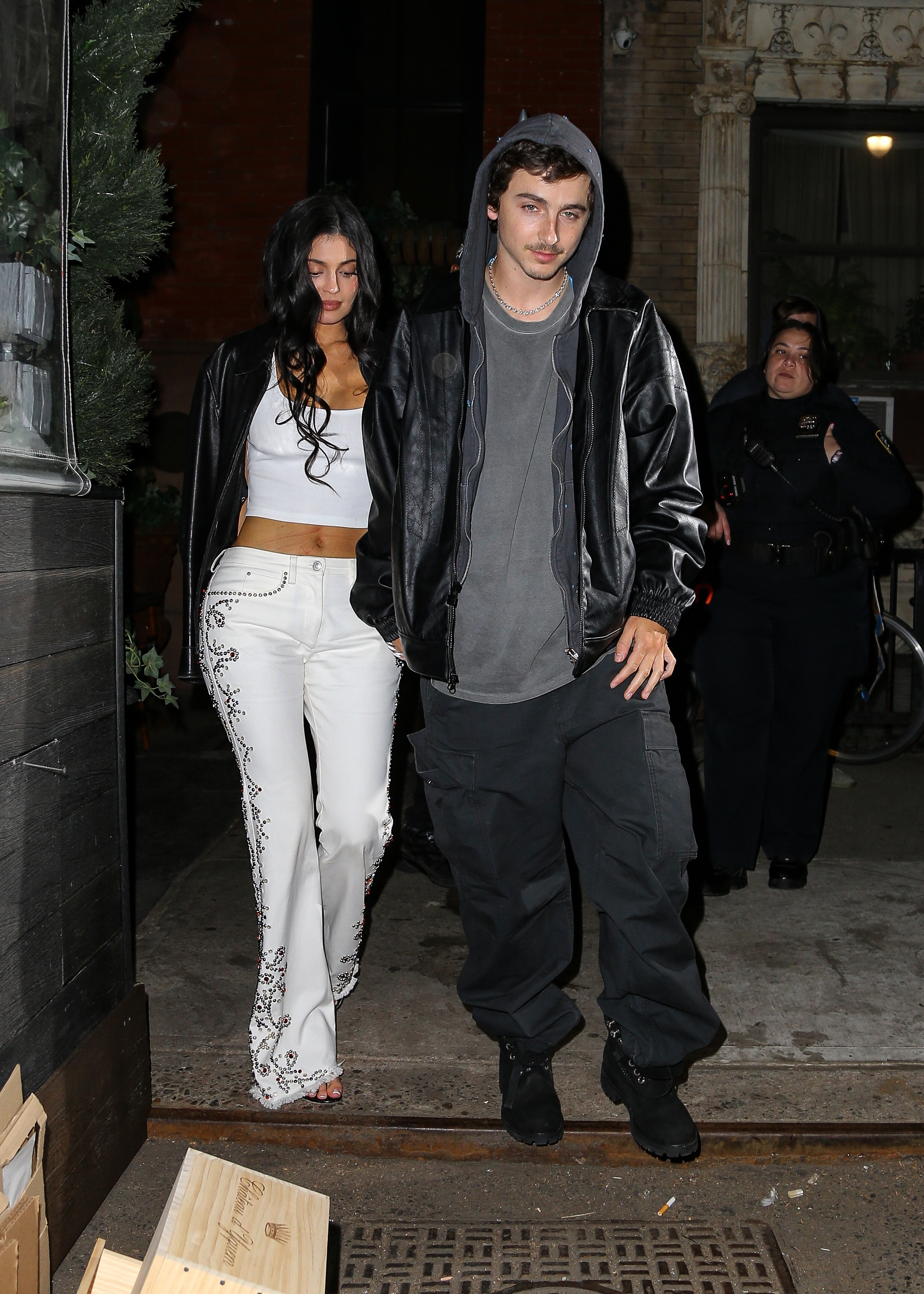 Kylie Jenner in a white outfit and Timothée Chalamet in a black outfit leave a steakhouse.