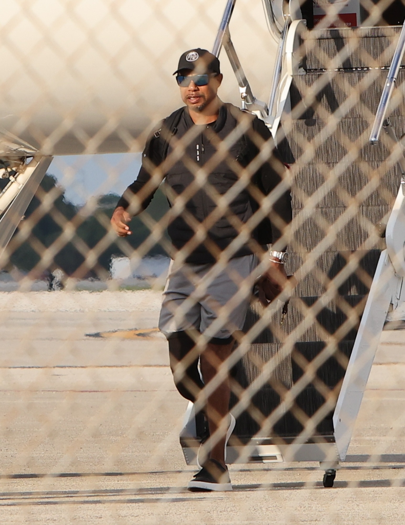 Tiger Woods disembarking a private jet, seen through a fence.