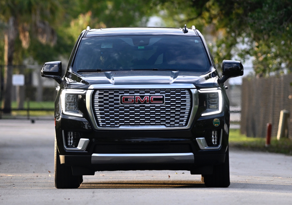 Front view of a black GMC vehicle with its headlights on, driving on a road.