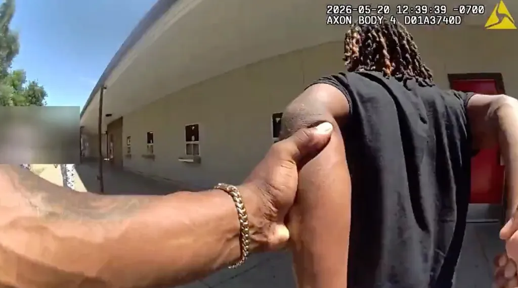 Bodycam footage shows a person with dreadlocks being held by their arm by a police officer.