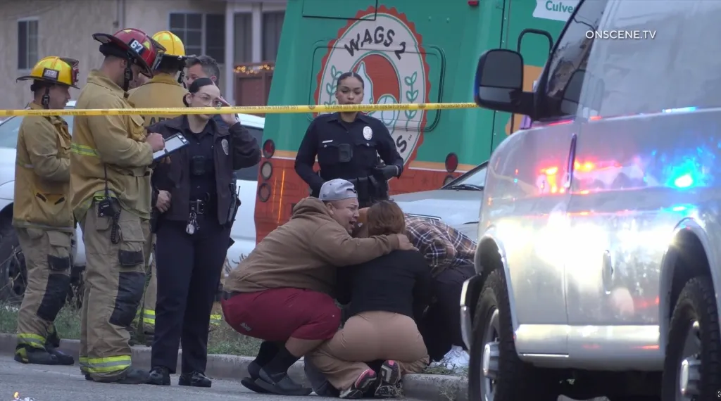 Family members crying and embracing at a crime scene, with police officers and firefighters nearby.